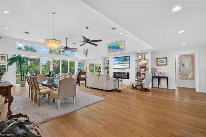 Expansive open-concept room featuring wood-finish flooring, a contemporary chandelier, multiple ceiling fans, a built-in fireplace, and large windows