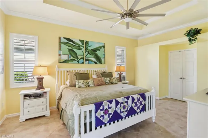 Bedroom with ornamental molding, a closet, ceiling fan, light tile patterned floors, and a raised ceiling