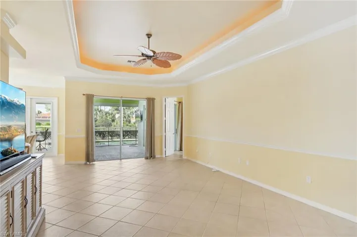 Empty room featuring a tray ceiling, a ceiling fan, light tile patterned floors, and crown molding
