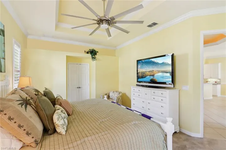 Bedroom featuring ornamental molding, a closet, a ceiling fan, light tile patterned floors, and a raised ceiling