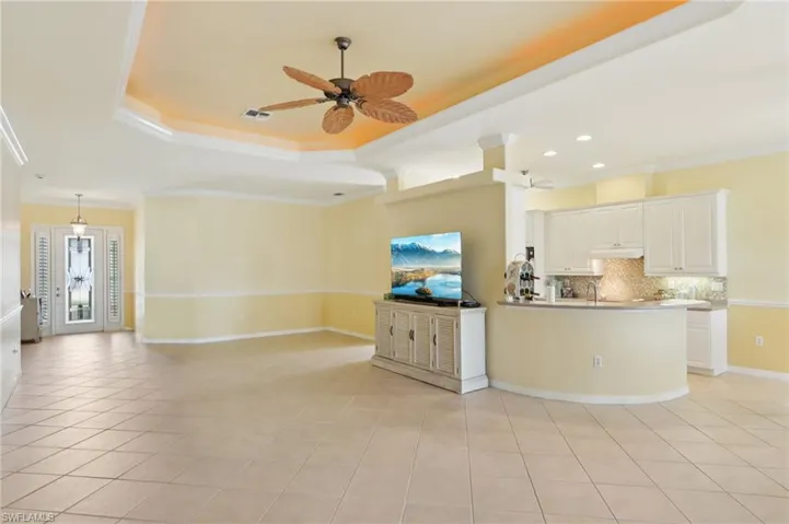 Kitchen with a raised ceiling, open floor plan, backsplash, ornamental molding, and white cabinets