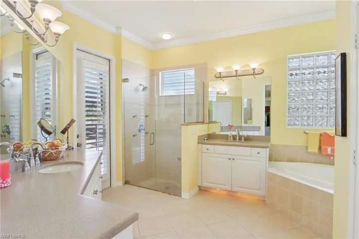 Full bath with two vanities, a stall shower, crown molding, light tile patterned floors, and a bath