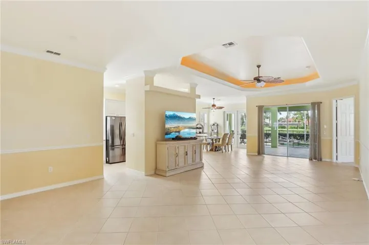 Living area featuring ornamental molding, a tray ceiling, light tile patterned flooring, and a ceiling fan