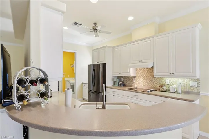 Kitchen featuring white cabinets, freestanding refrigerator, crown molding, decorative backsplash, and under cabinet range hood