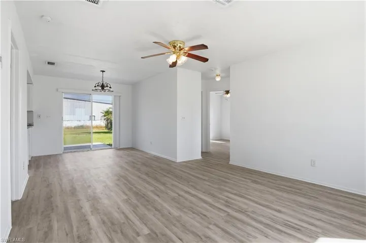 Empty room with light wood-type flooring, ceiling fan, and a chandelier