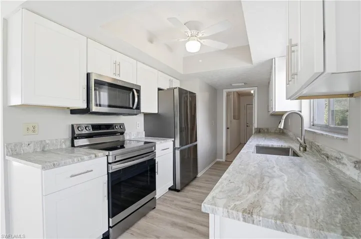 Kitchen featuring appliances with stainless steel finishes, white cabinetry, light stone countertops, and a tray ceiling