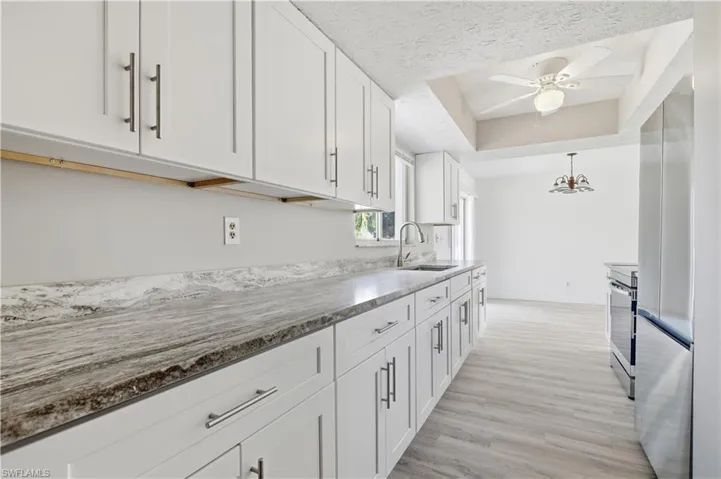 Kitchen with white cabinets, stainless steel appliances, light wood-style floors, a tray ceiling, and a textured ceiling