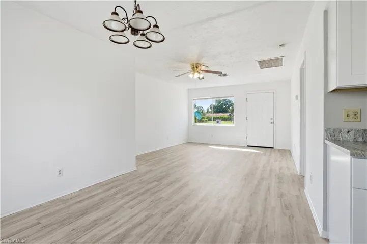 Unfurnished living room featuring light wood finished floors, a chandelier, a ceiling fan, and a textured ceiling