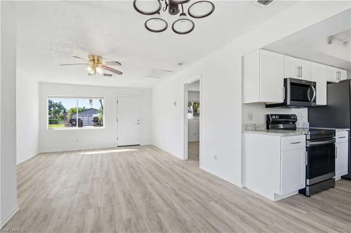 Kitchen with stainless steel appliances, white cabinets, ceiling fan, light wood-style floors, and a textured ceiling