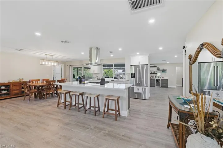 Open Concept Kitchen with stainless steel refrigerator with ice dispenser, light quartz counters, LVP floors, wine cooler, and white cabinetry