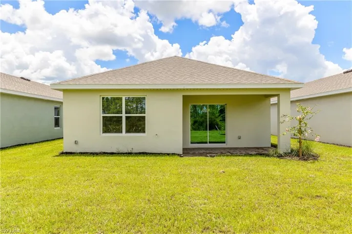 Back of house featuring a lawn, stucco siding, and roof with shingles