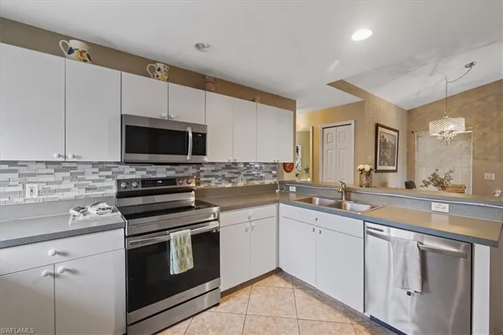 Kitchen with stainless steel appliances, a sink, a chandelier, decorative backsplash, and white cabinetry