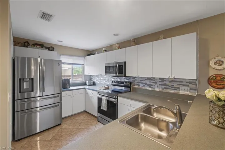 Kitchen featuring appliances with stainless steel finishes, a sink, light tile patterned flooring, tasteful backsplash, and white cabinets