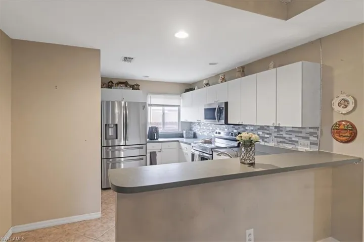 Kitchen with stainless steel appliances, a peninsula, decorative backsplash, white cabinetry, and light tile patterned floors
