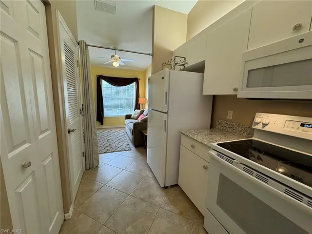 Kitchen with white cabinets, ceiling fan, white appliances, and light tile patterned floors