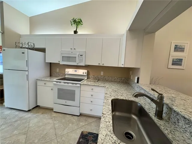 Kitchen featuring light stone countertops, white appliances, sink, light tile patterned floors, and white cabinets
