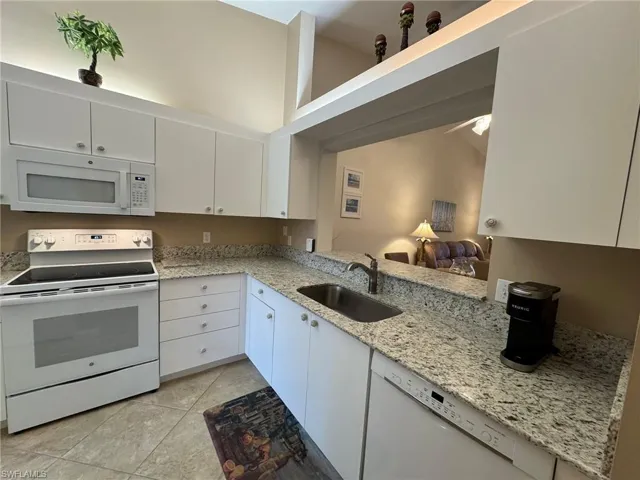 Kitchen with sink, light tile patterned floors, kitchen peninsula, white appliances, and white cabinets