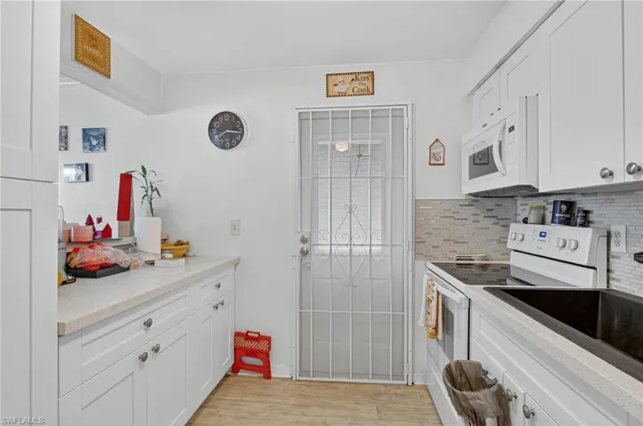 Kitchen with white appliances, white cabinets, light wood finished floors, tasteful backsplash, and light stone countertops
