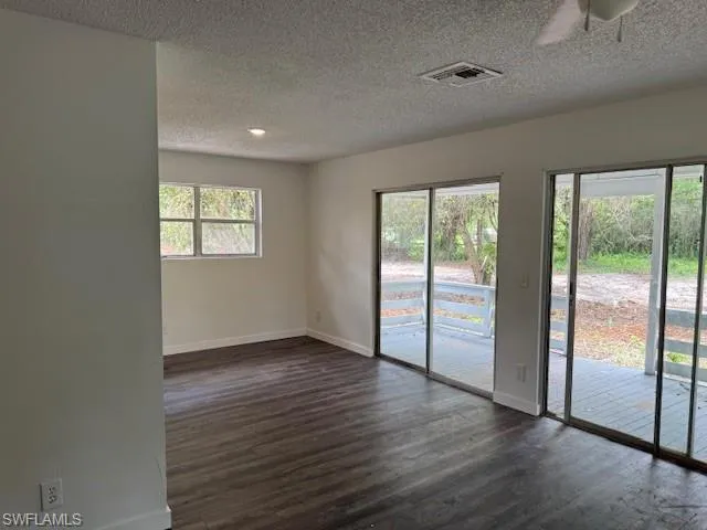 Unfurnished room with a textured ceiling, dark wood-style floors, and a ceiling fan