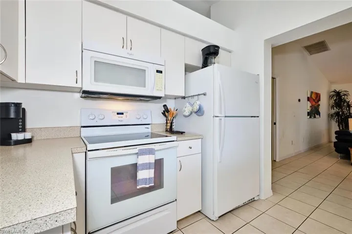 Kitchen with white appliances, light countertops, white cabinetry, and light tile patterned flooring