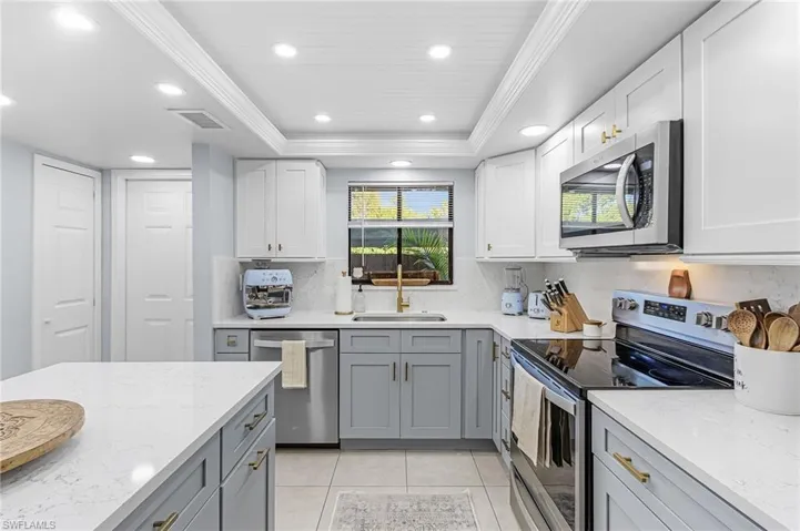 Dual tone kitchen featuring stainless steel appliances, light stone countertops, a tray ceiling, ornamental molding, and dual tone cabinetry