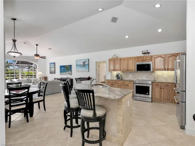Kitchen with lofted ceiling, light stone countertops, light tile patterned floors, stainless steel appliances, and open floor plan