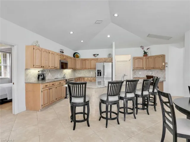 Kitchen with stainless steel appliances, backsplash, lofted ceiling, an island with sink, and light stone counters