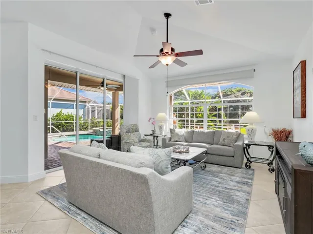 Living room with a sunroom, light tile patterned flooring, vaulted ceiling, and ceiling fan