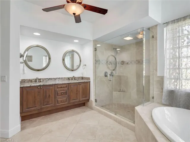 Full bath featuring double vanity, a bath, light tile patterned floors, a stall shower, and a ceiling fan