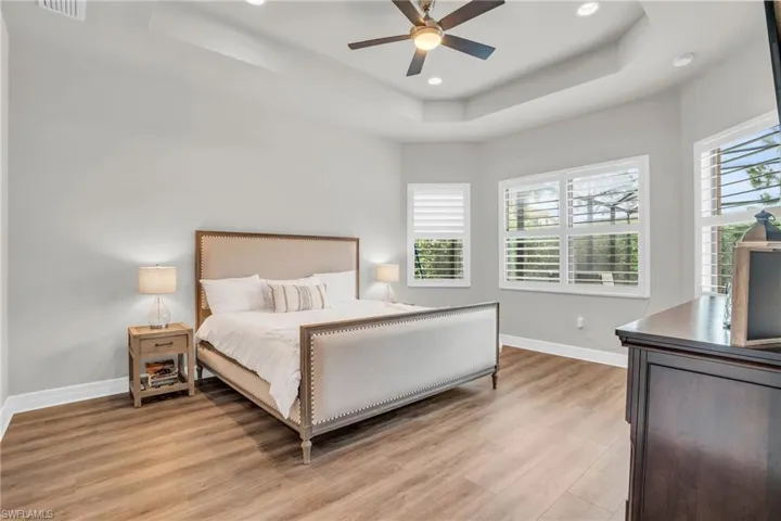 Bedroom featuring ceiling fan, a tray ceiling, and light wood-type flooring