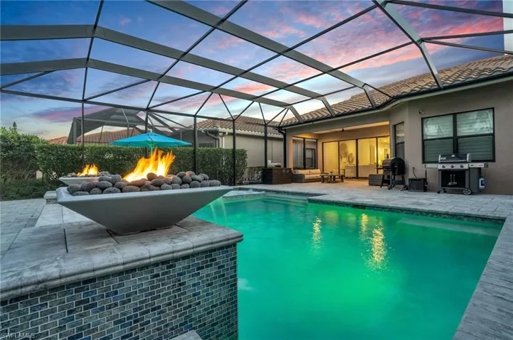 Pool at dusk featuring a patio, glass enclosure, and a grill
