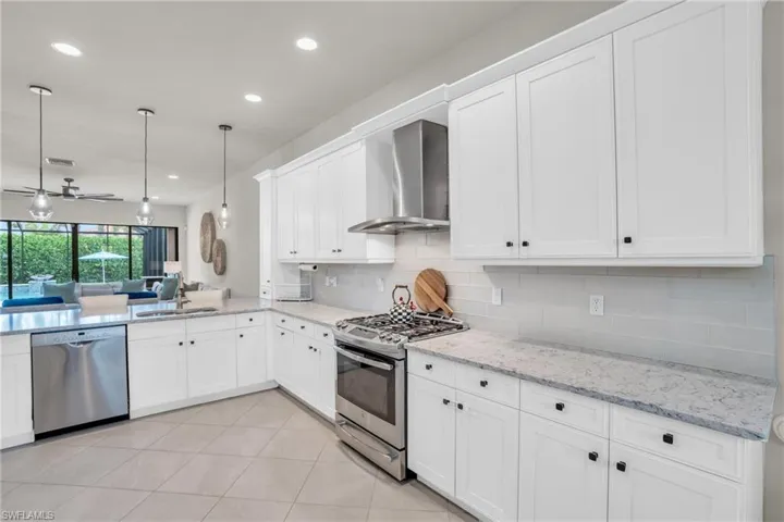 Kitchen with white cabinetry, appliances with stainless steel finishes, wall chimney exhaust hood, tasteful backsplash, and light tile floors
