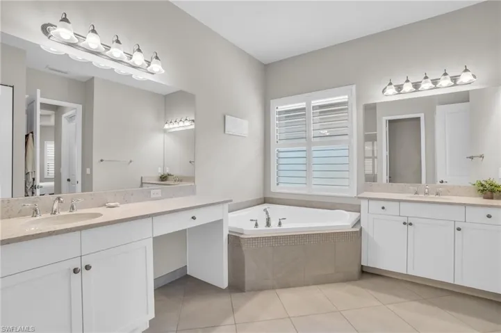 Bathroom featuring tiled bath, dual vanity, and tile flooring