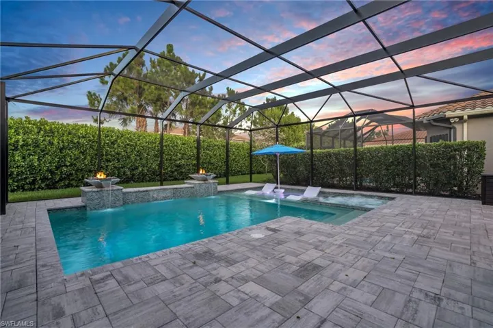 Pool at dusk featuring a patio area, glass enclosure, a hot tub, and pool water feature