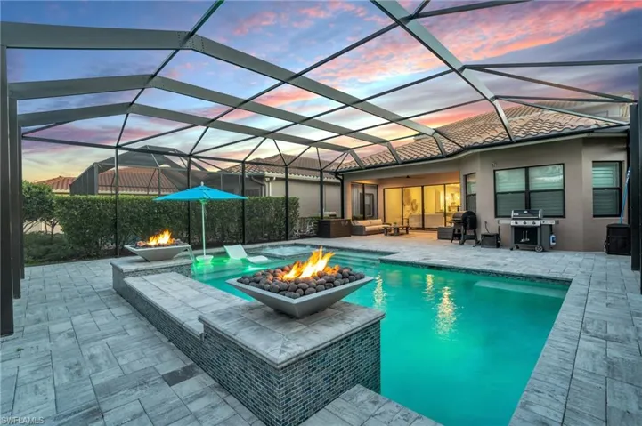 Pool at dusk with a fire pit, a grill, a lanai, and a patio