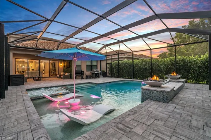 Pool at dusk featuring pool water feature, grilling area, a lanai, and a patio