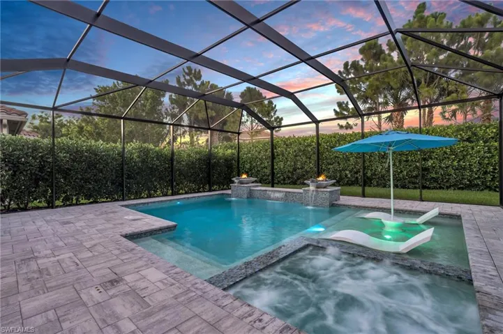 Pool at dusk with a patio, glass enclosure, an in ground hot tub, and pool water feature