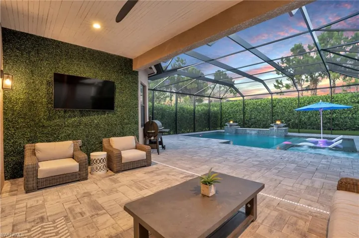 Pool at dusk featuring glass enclosure, an in ground hot tub, a patio area, pool water feature, and area for grilling