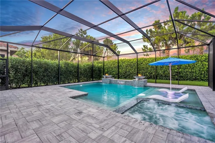 Pool at dusk featuring pool water feature, a lanai, an in ground hot tub, and a patio area