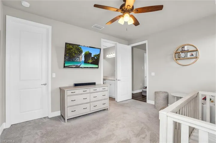 Bedroom with light carpet, a nursery area, ensuite bathroom, and ceiling fan