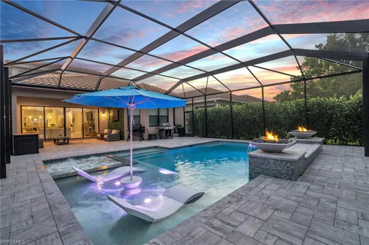 Pool at dusk featuring pool water feature, glass enclosure, an in ground hot tub, and a patio