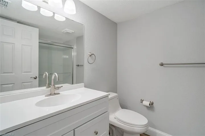Full bath with a textured wall, a shower with shower door, vanity, and a textured ceiling