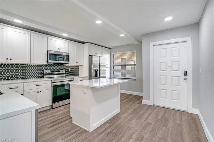 Kitchen with appliances with stainless steel finishes, light countertops, light wood-type flooring, white cabinets, and tasteful backsplash