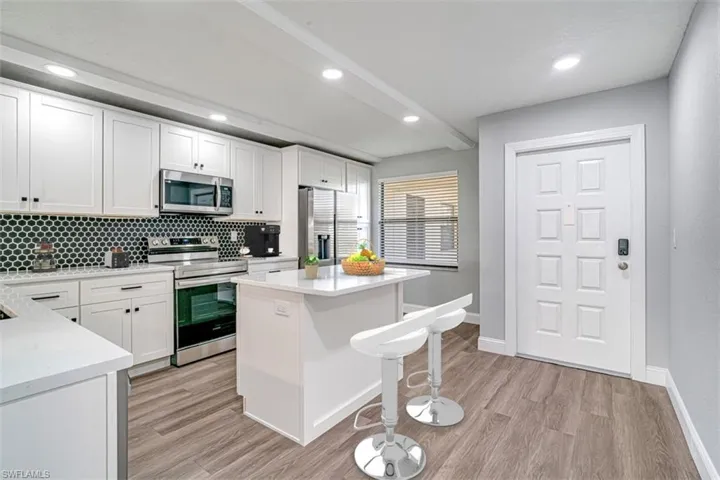 Kitchen with appliances with stainless steel finishes, a breakfast bar, light countertops, decorative backsplash, and white cabinets