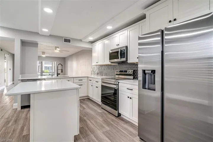 Kitchen featuring stainless steel appliances, light countertops, a peninsula, tasteful backsplash, and light wood-style flooring