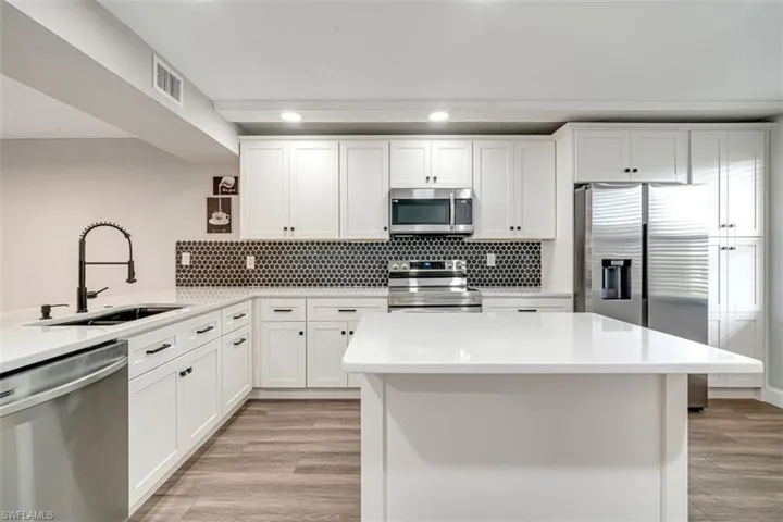 Kitchen with appliances with stainless steel finishes, backsplash, light wood finished floors, white cabinetry, and recessed lighting