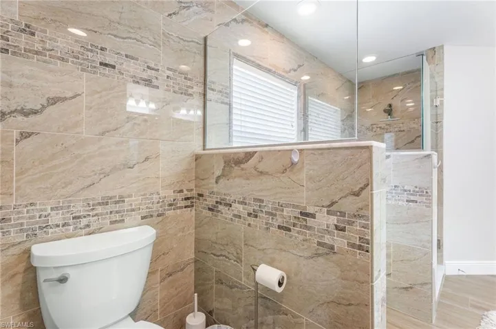 Bathroom featuring a walk in shower, toilet, tile walls, and recessed lighting