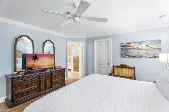 Bedroom featuring ornamental molding, ceiling fan, wood finished floors, baseboards, and connected bathroom