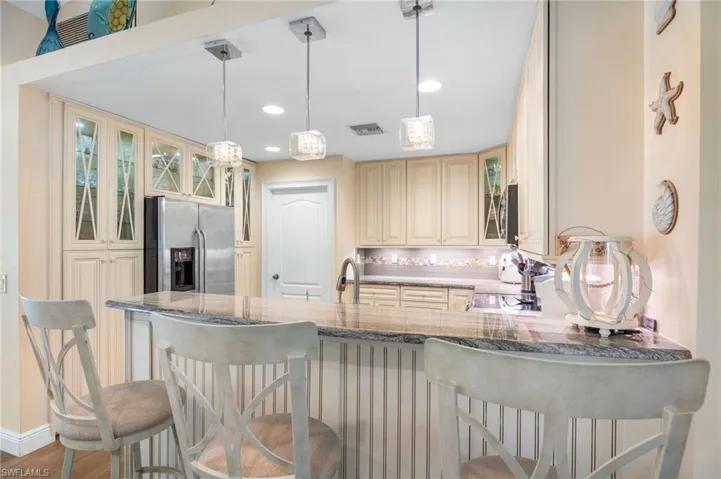 Kitchen with stainless steel fridge with ice dispenser, cream cabinetry, a peninsula, light stone counters, and pendant lighting