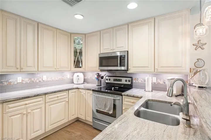 Kitchen with stainless steel appliances, cream cabinetry, a sink, backsplash, and light stone countertops